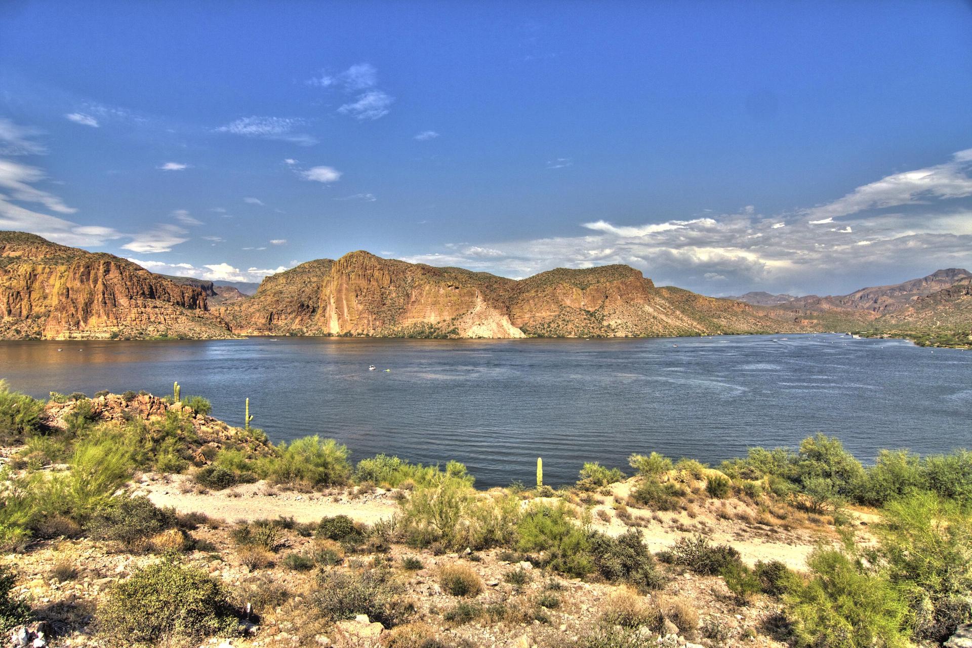Wide lake surrounded by desert mountains and scrub under a bright blue sky.