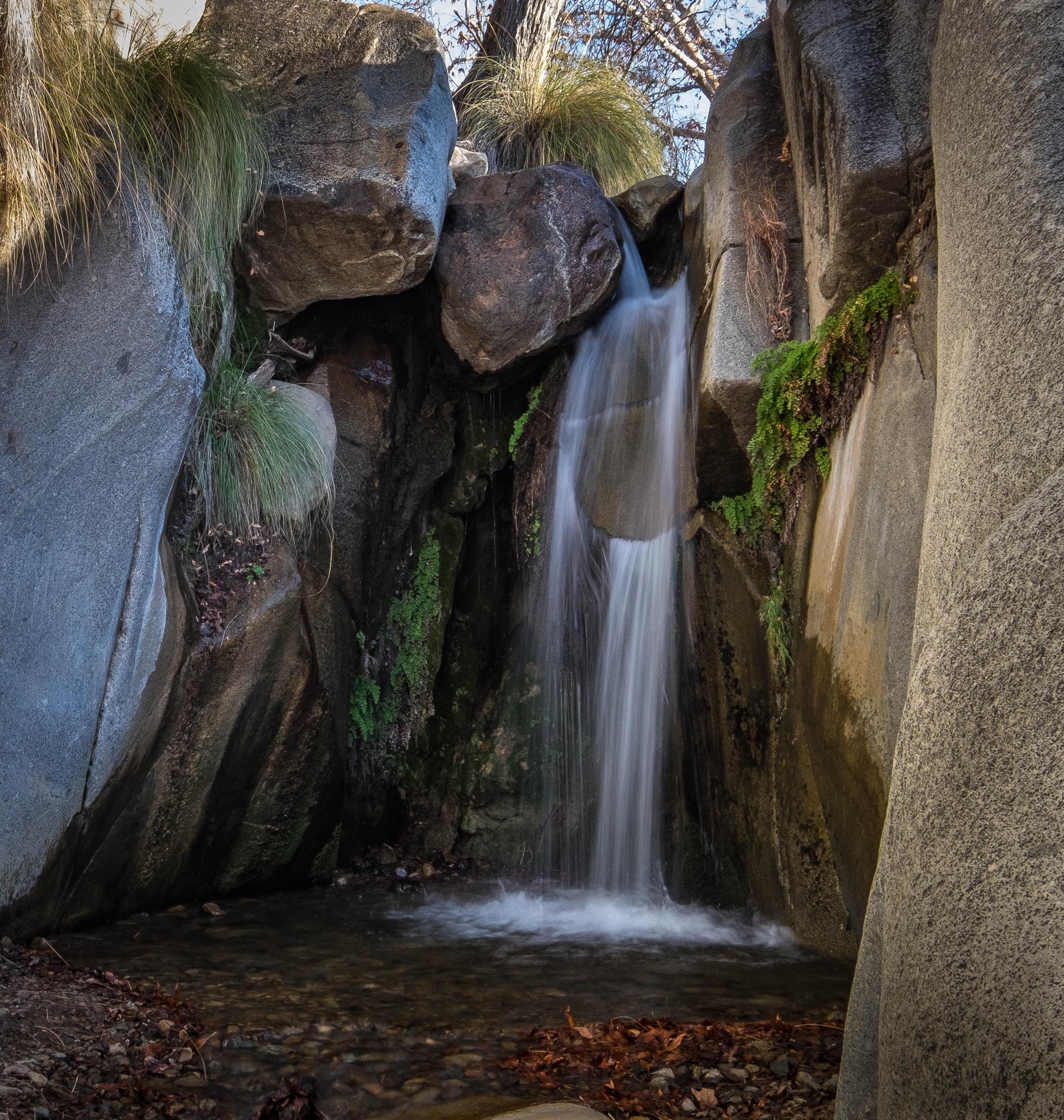 A beautiful waterfall cascades into a rocky pool surrounded by green moss and grass.