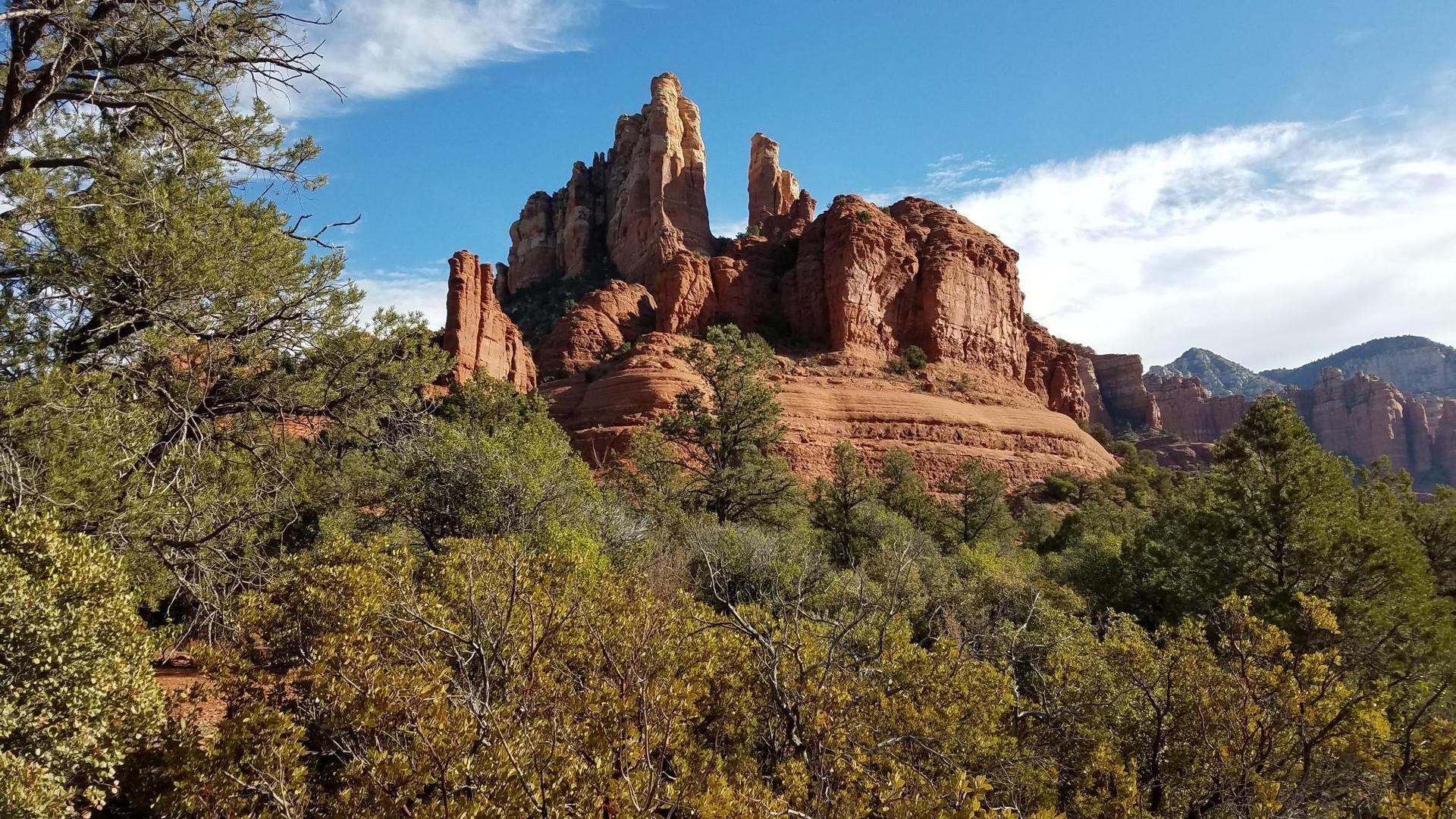 Majestic red rock formations towering over green trees under a blue sky.