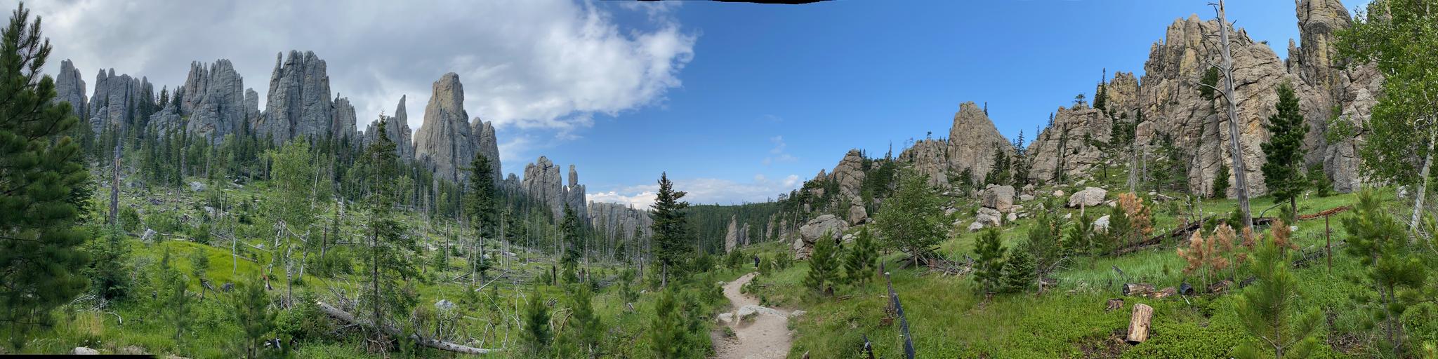 Dirt path winding through a valley surrounded by tall rocky spires and green trees.