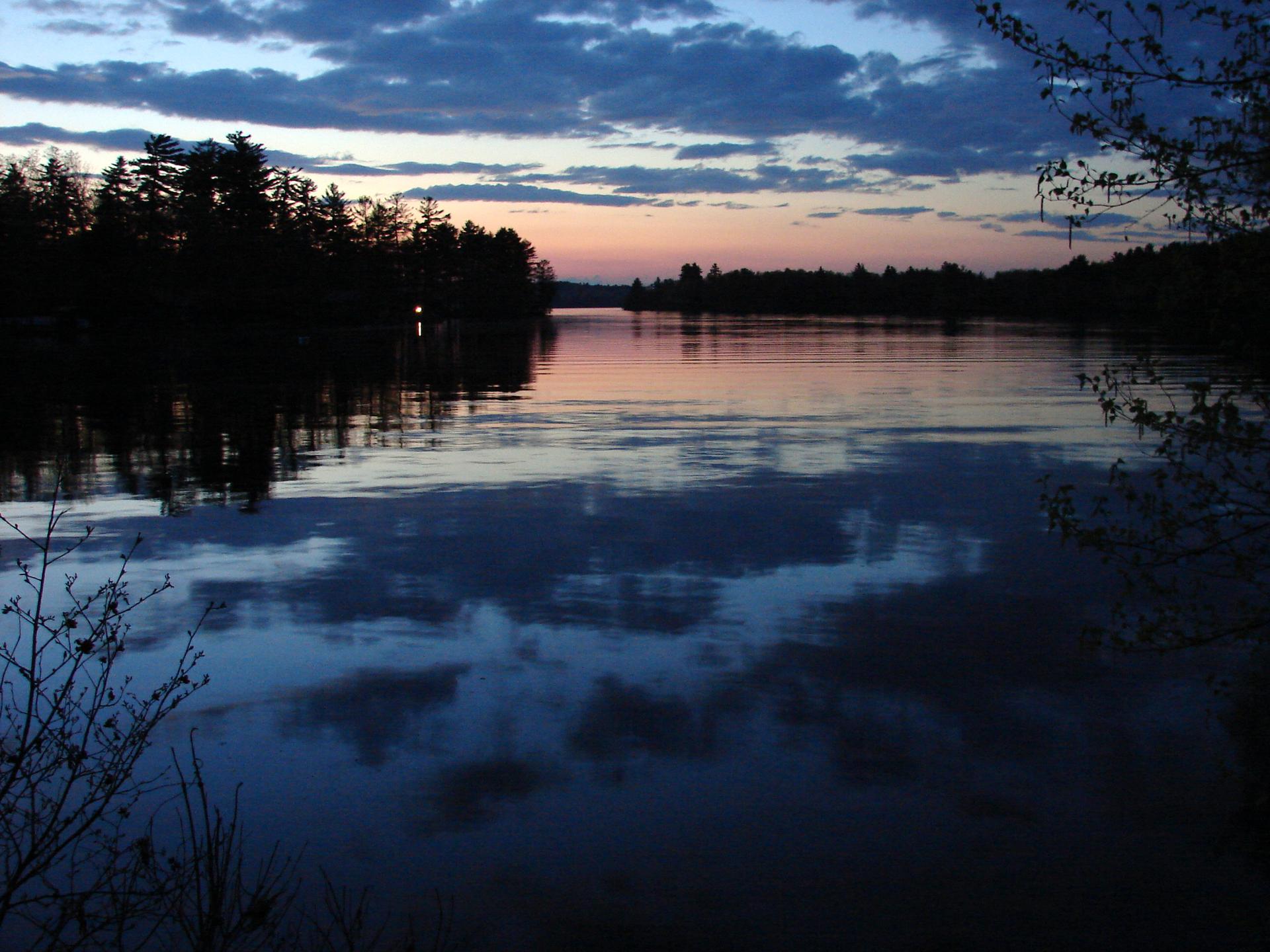 Serene lake at twilight, with silhouetted trees and cloudy sky reflections.
