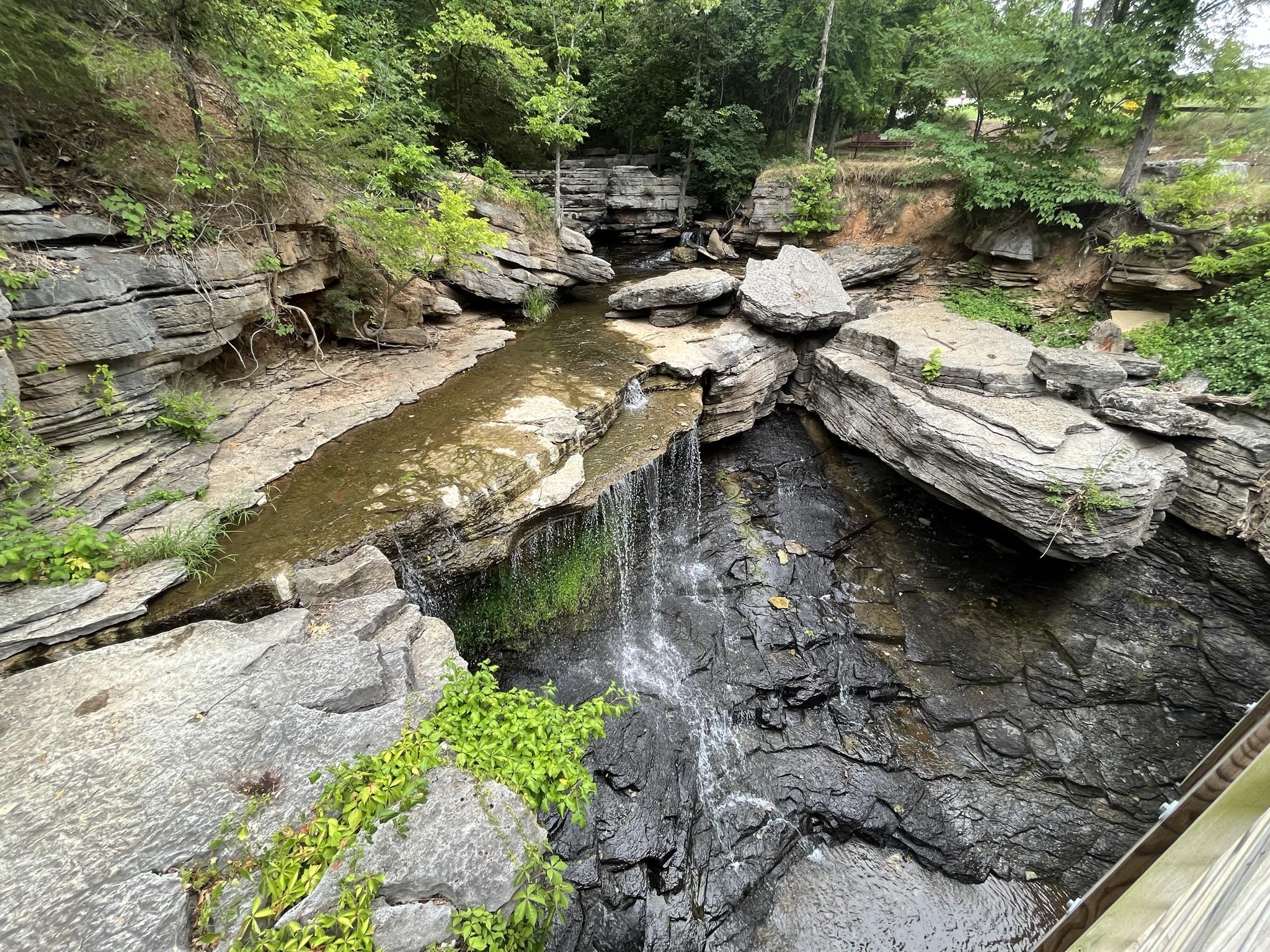 A small waterfall plunging into a dark pool surrounded by layered rock formations.