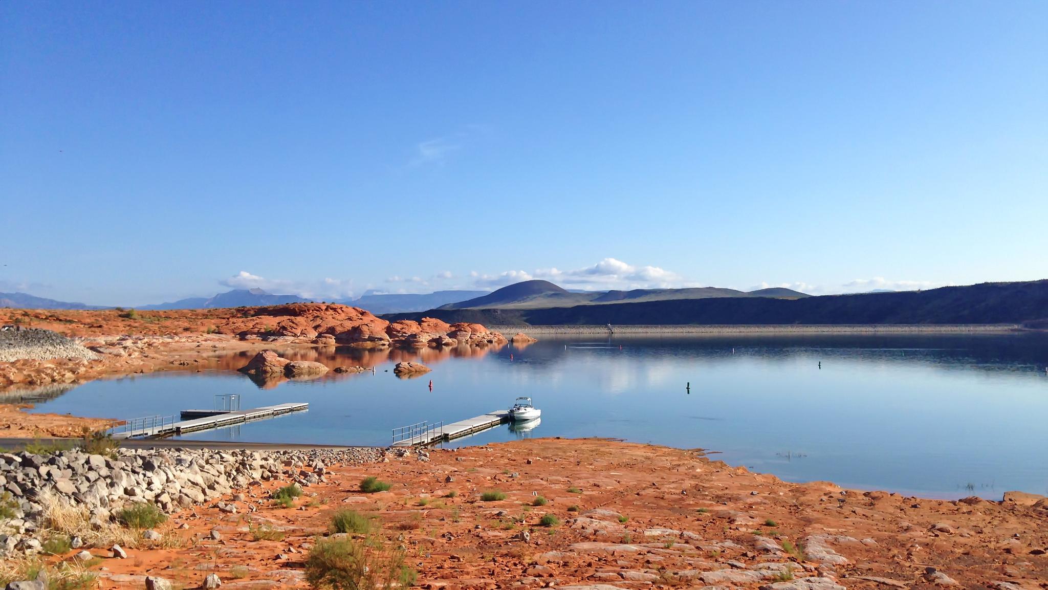 Clear blue sky over a lake, boat dock, and red rocky landscape.