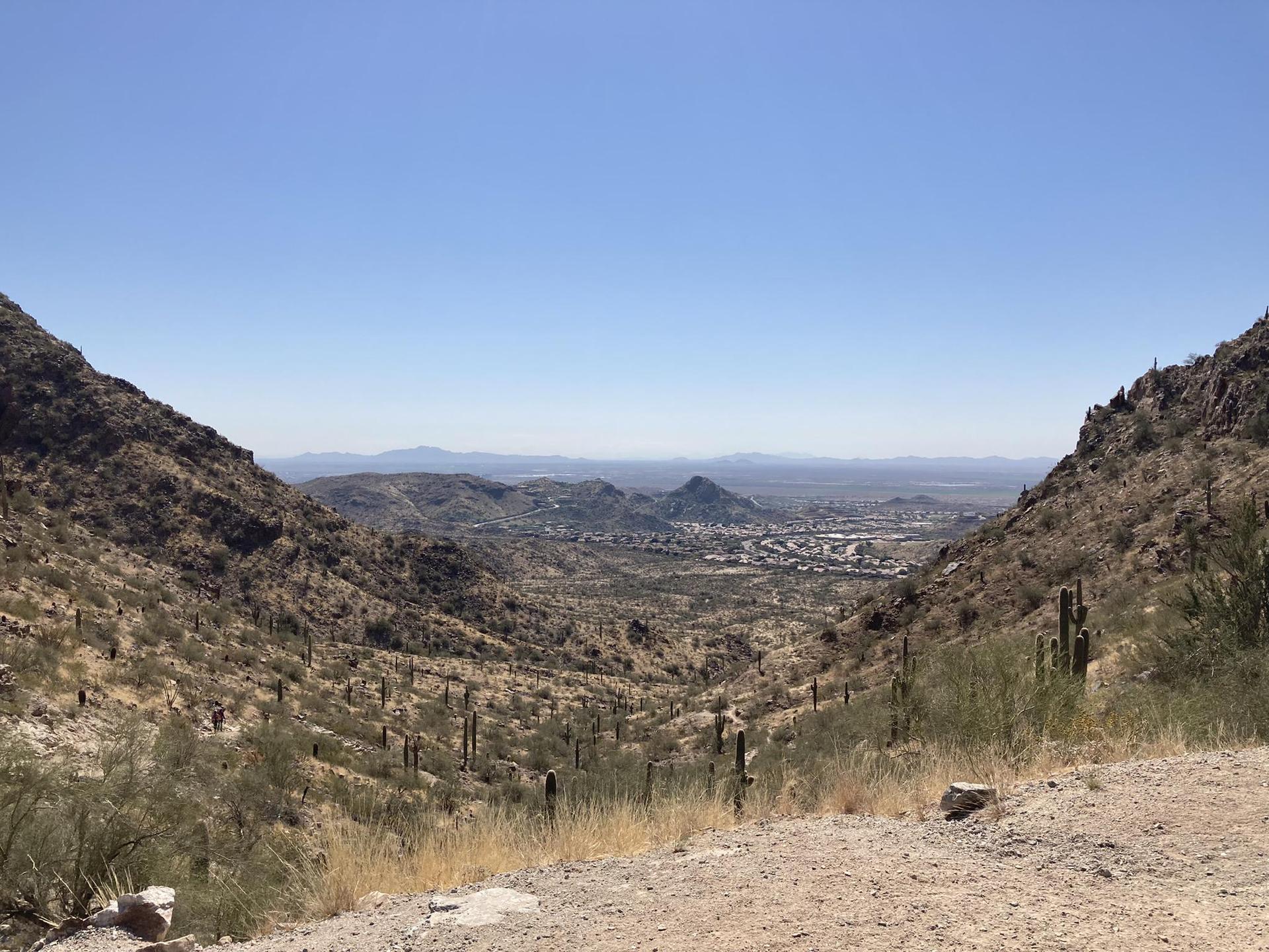 Expansive desert valley view with mountains and distant city under clear sky.