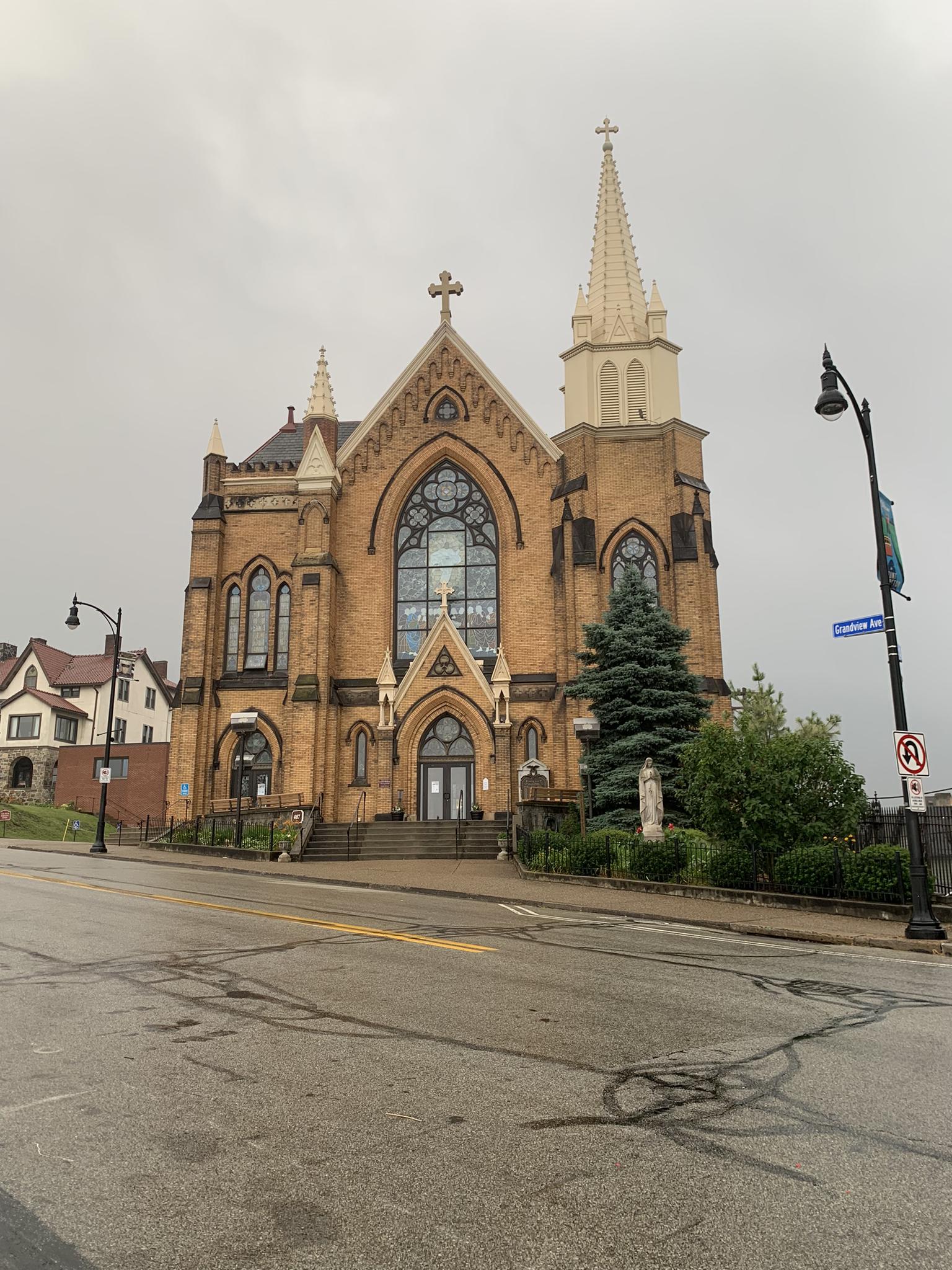 Ornate brick church with a tall steeple on a cloudy day.