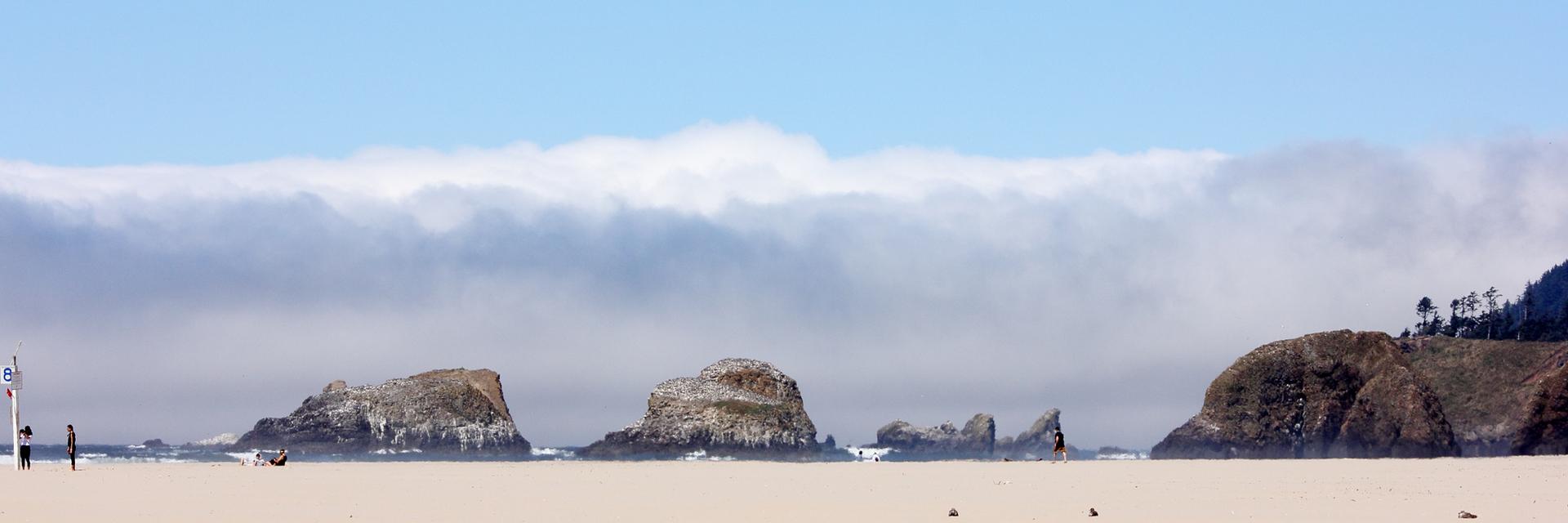 Wide sandy beach with sea stacks and a low cloud bank over the ocean.