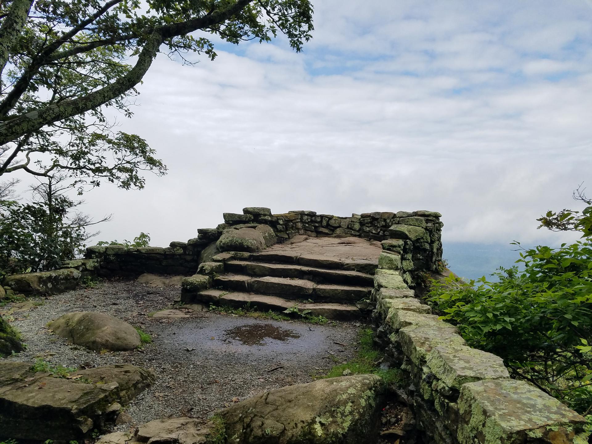 Stone observation platform with steps overlooking a misty, tree-filled landscape.
