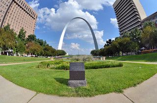 Fisheye view of a large arch, green lawn, and tall city buildings. - Gateway Arch and Riverfront Trail