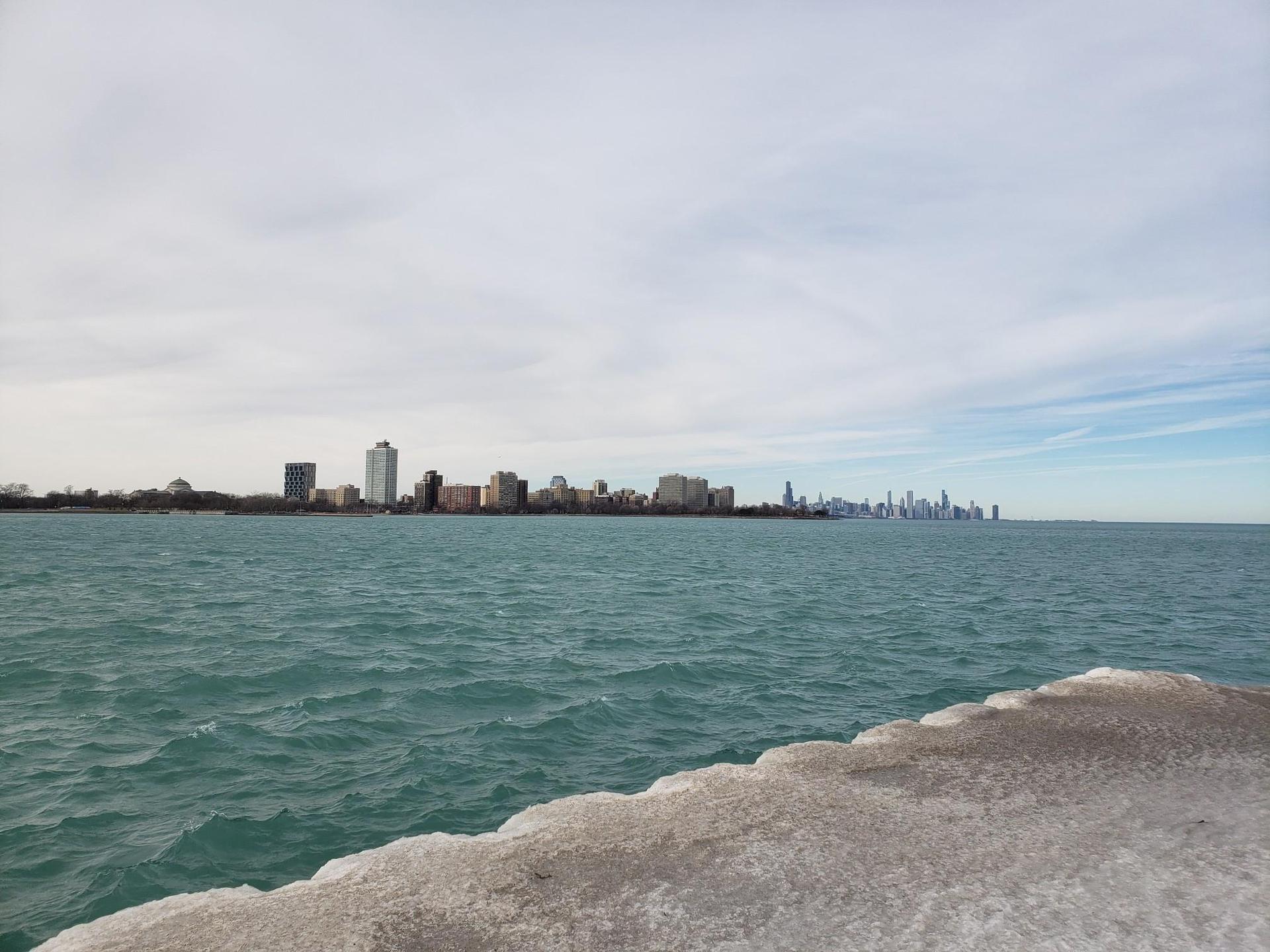 Wide view of a large body of water with a distant city skyline under cloudy sky.