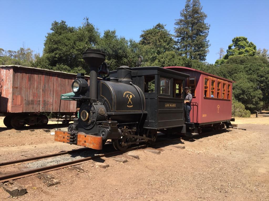 A black steam locomotive and red passenger car on tracks with a person.