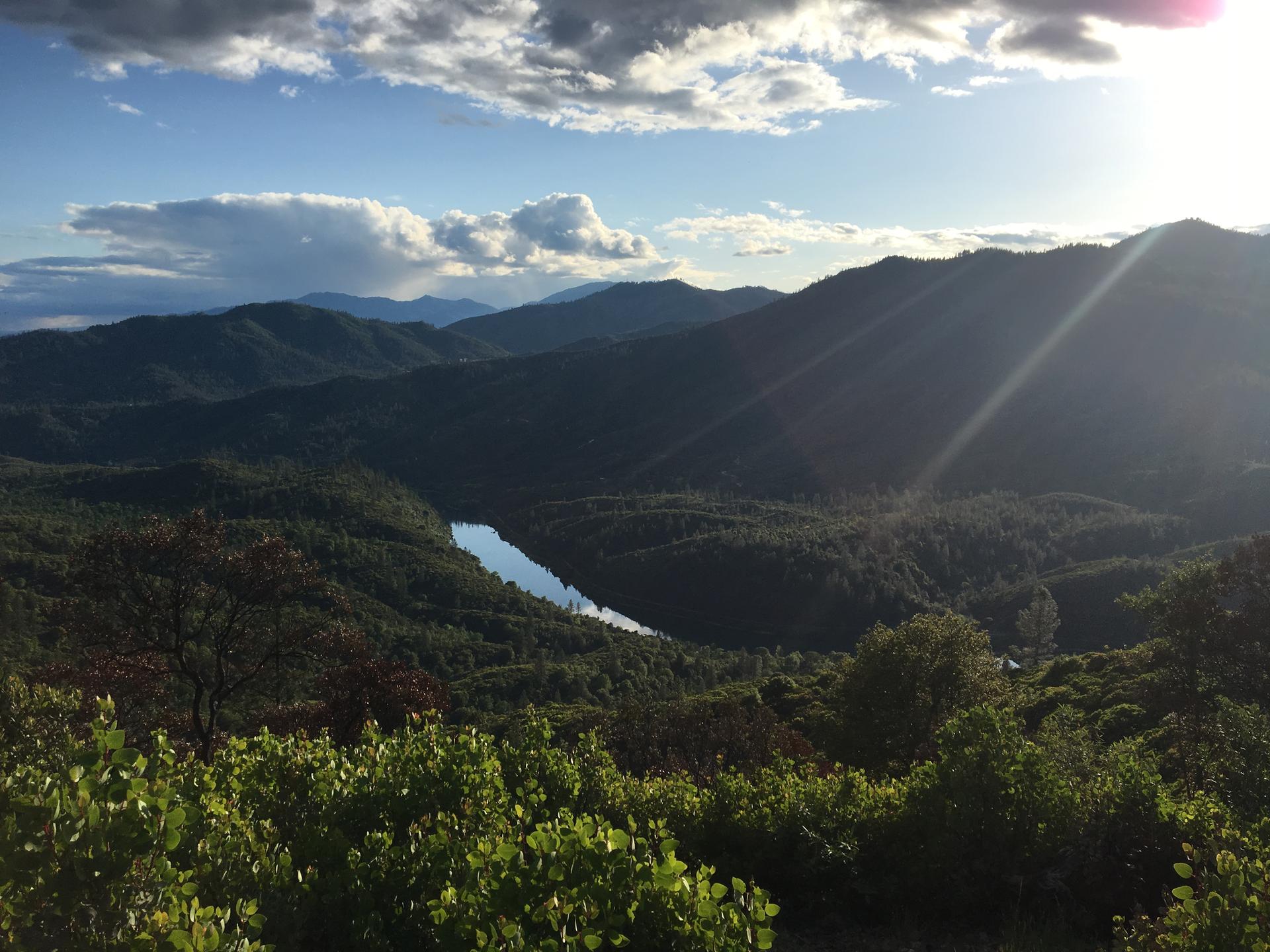 Dramatic sunset over a forested mountain landscape with a serene lake below.