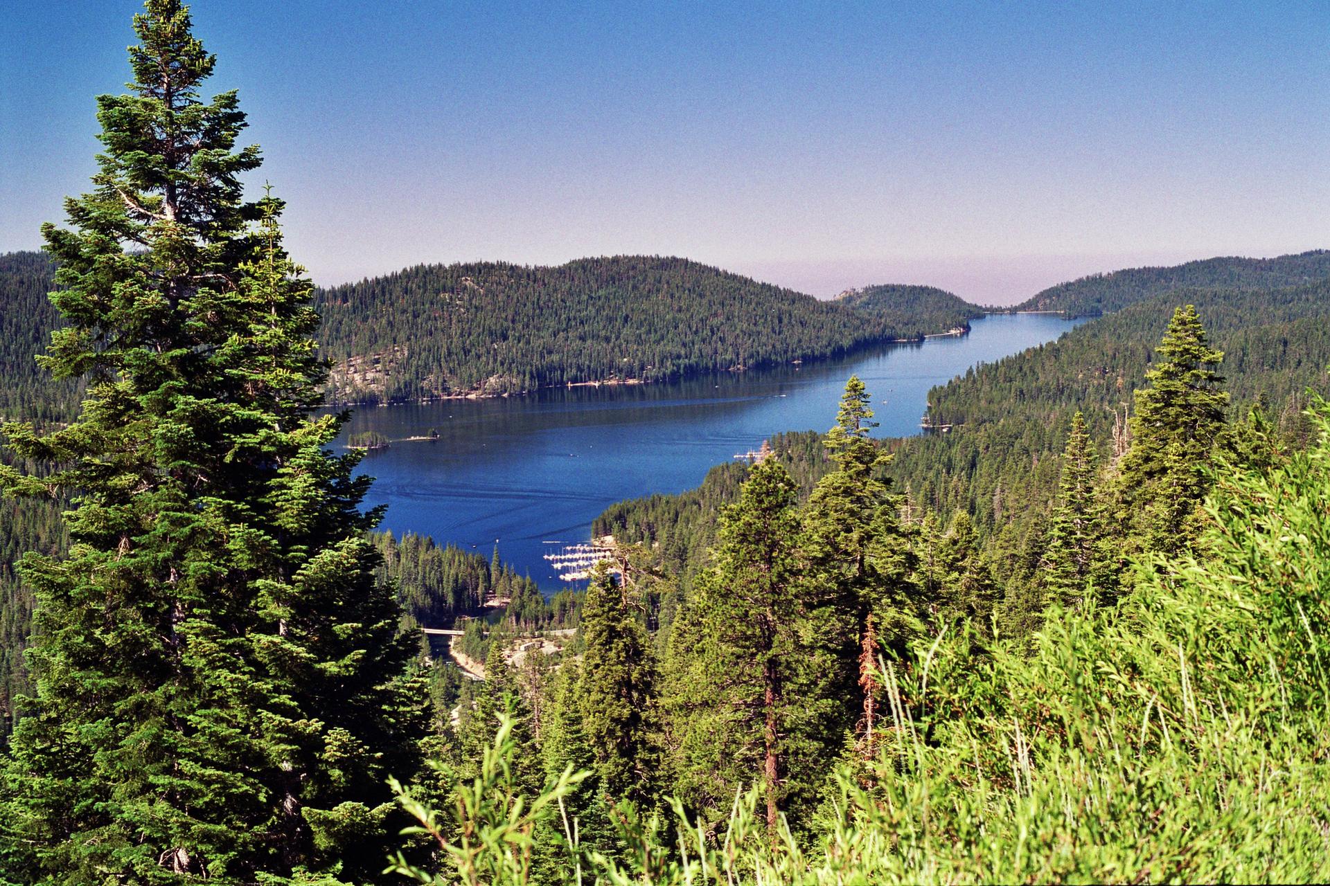 Panoramic view of a mountain lake with boats, surrounded by dense green forests.