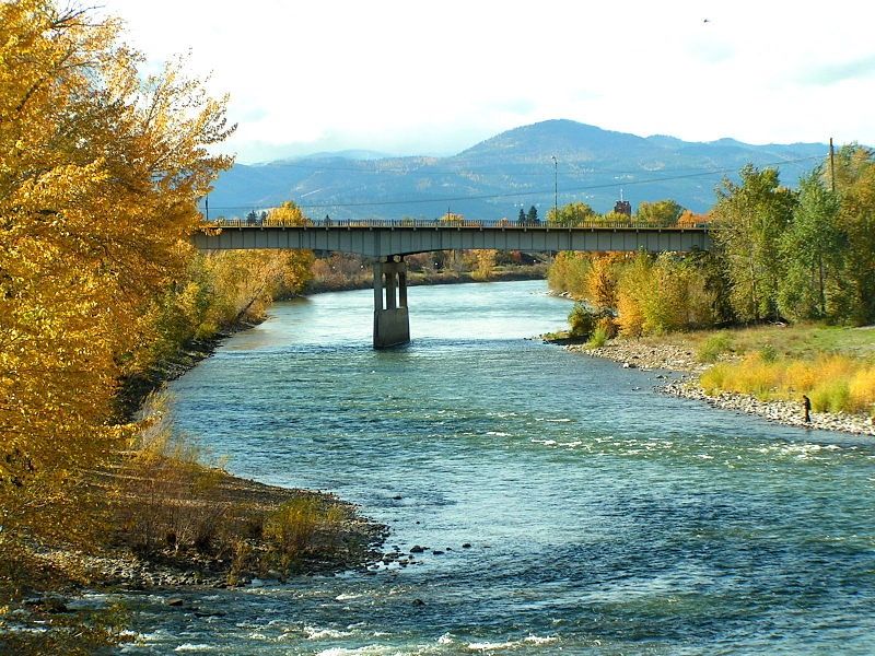 River flows under a bridge, flanked by vibrant autumn trees and distant mountains. - Missoula/Clark Fork River loop