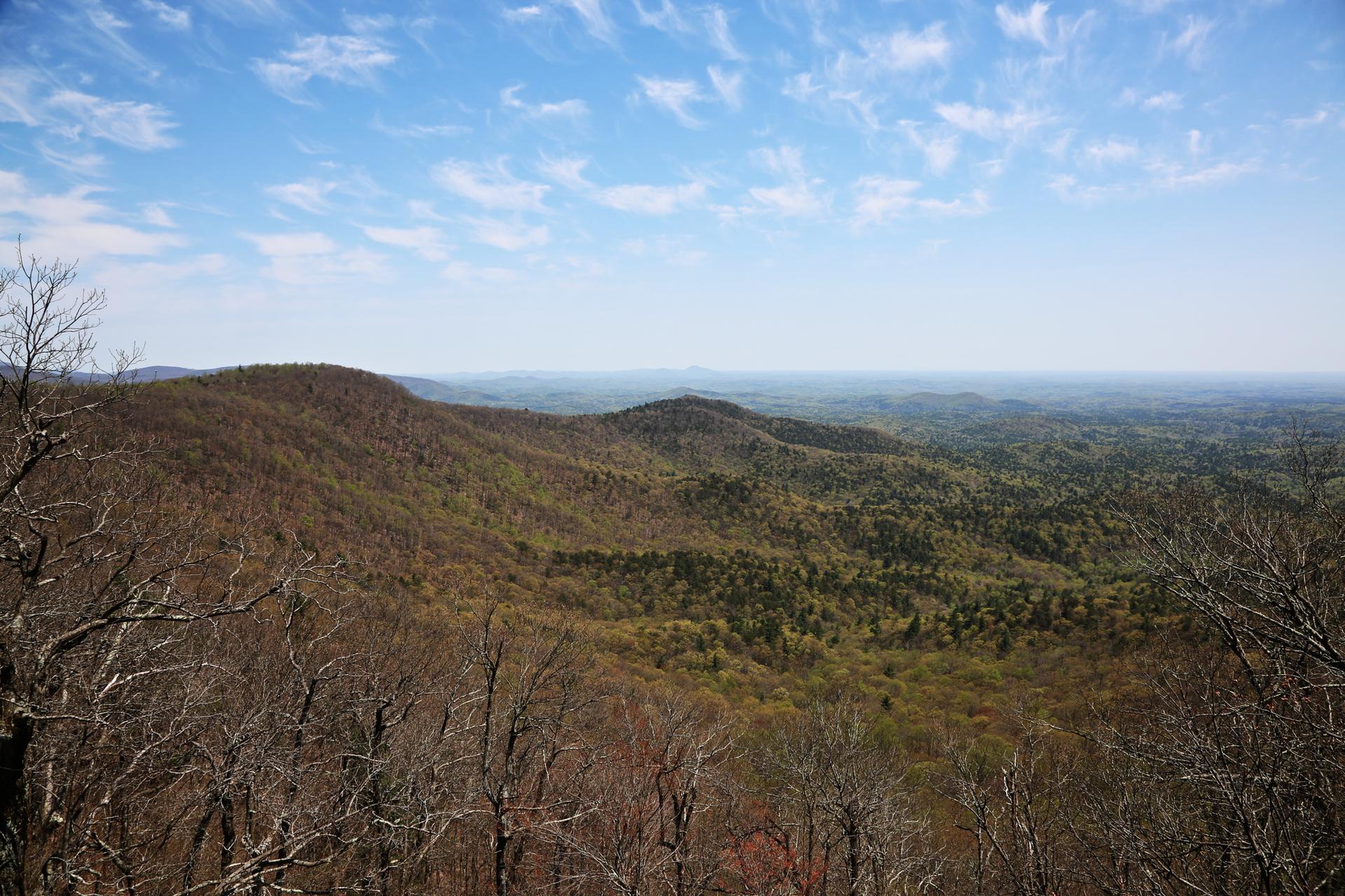 Panoramic view of rolling forested hills under a bright, partly cloudy sky.