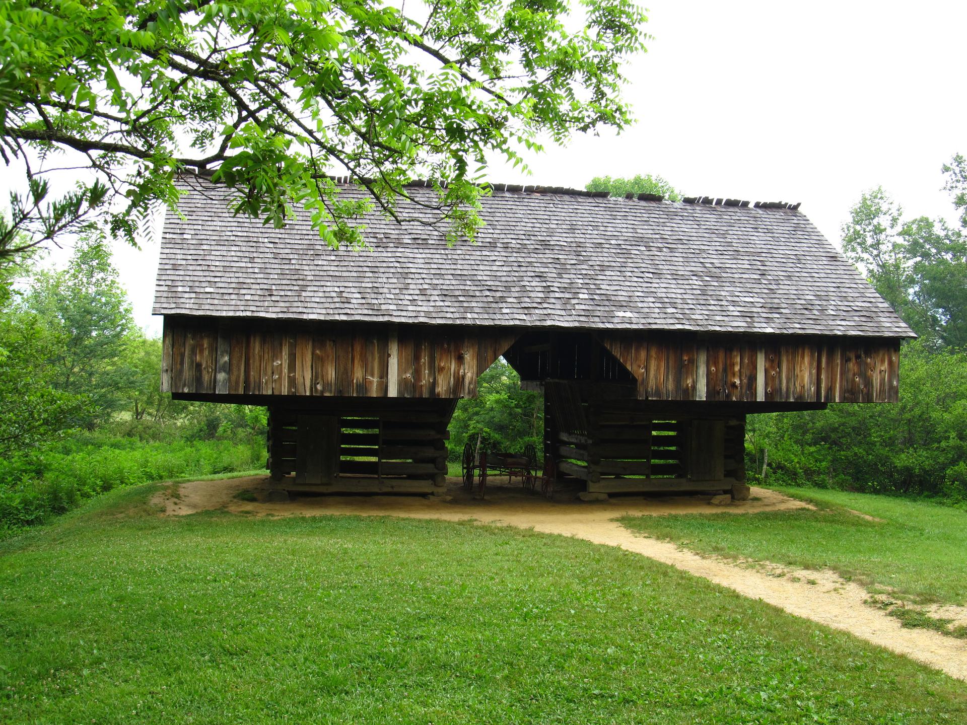 Historic wooden barn on stilts with a shingled roof, surrounded by green grass.