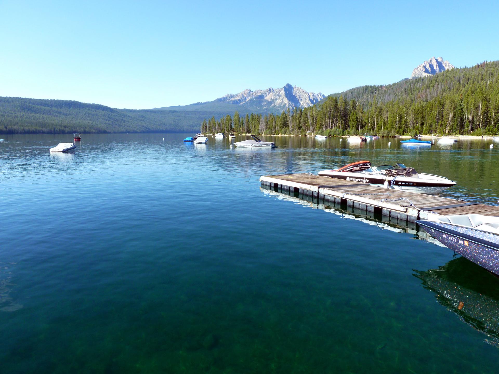 Boats on a clear blue lake with forested mountains under a sunny sky.