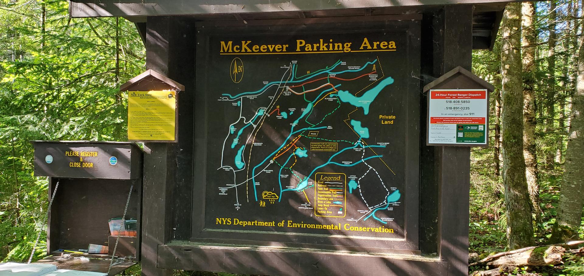 Wooden information sign with a map surrounded by green forest foliage.