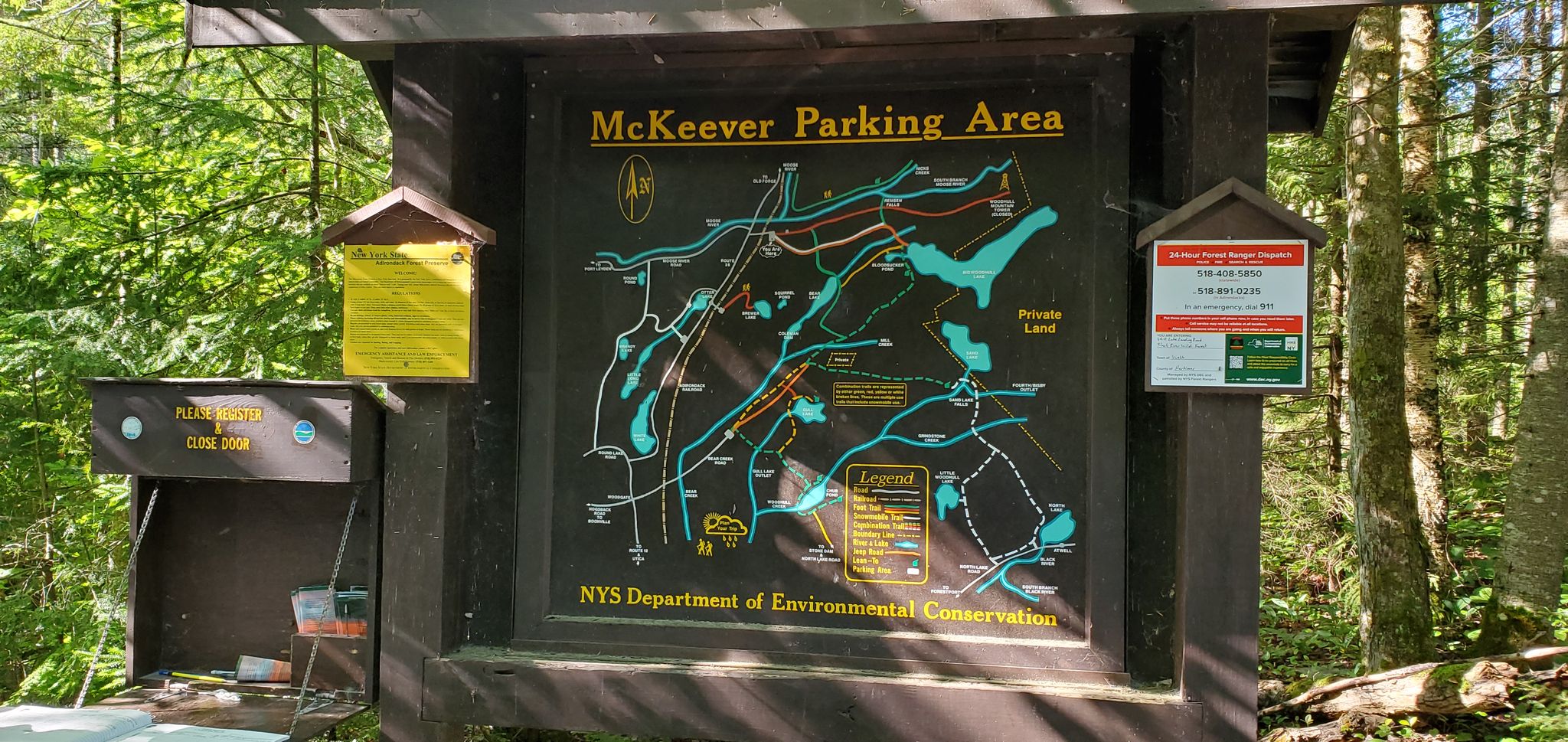 Wooden information sign with a map surrounded by green forest foliage. - Bear Lake Trail