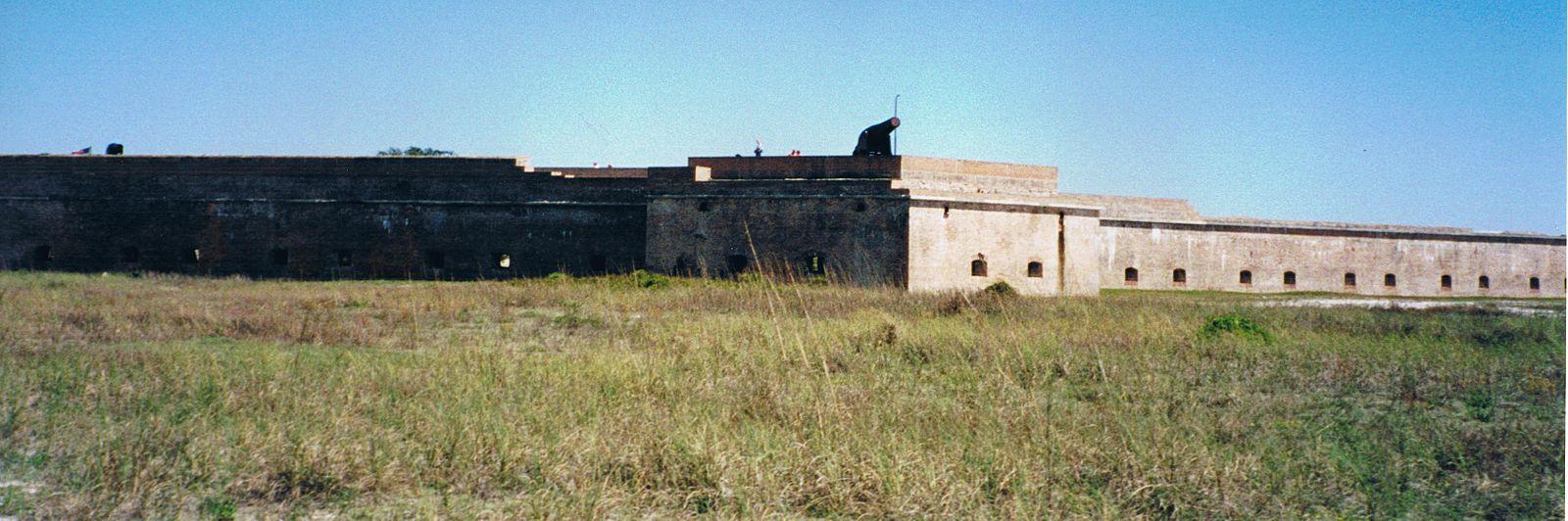 Long, ancient stone fort wall in a dry grassy field under clear sky.
