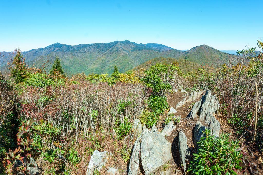 Rocky, shrub-covered foreground with distant green mountains under a clear blue sky.