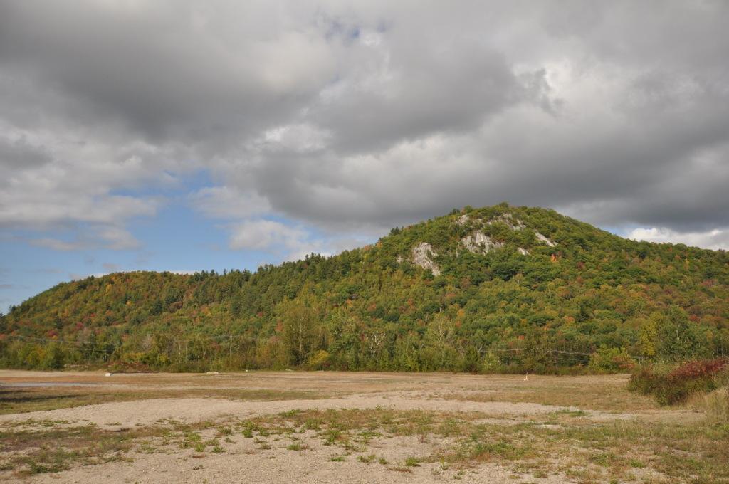 Forested hills under a cloudy sky, with a barren, sandy foreground.