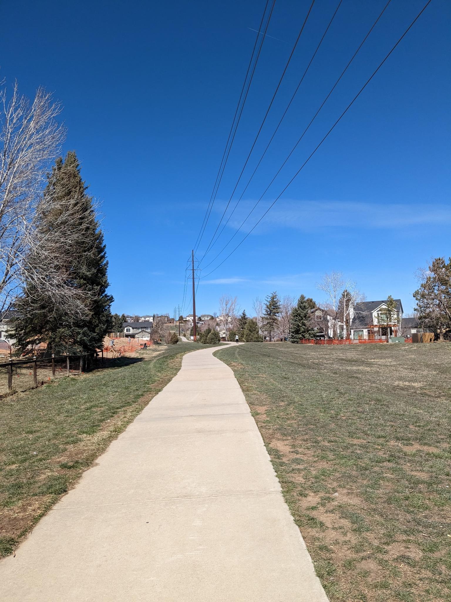 Paved path curving through a grassy field under a clear blue sky.