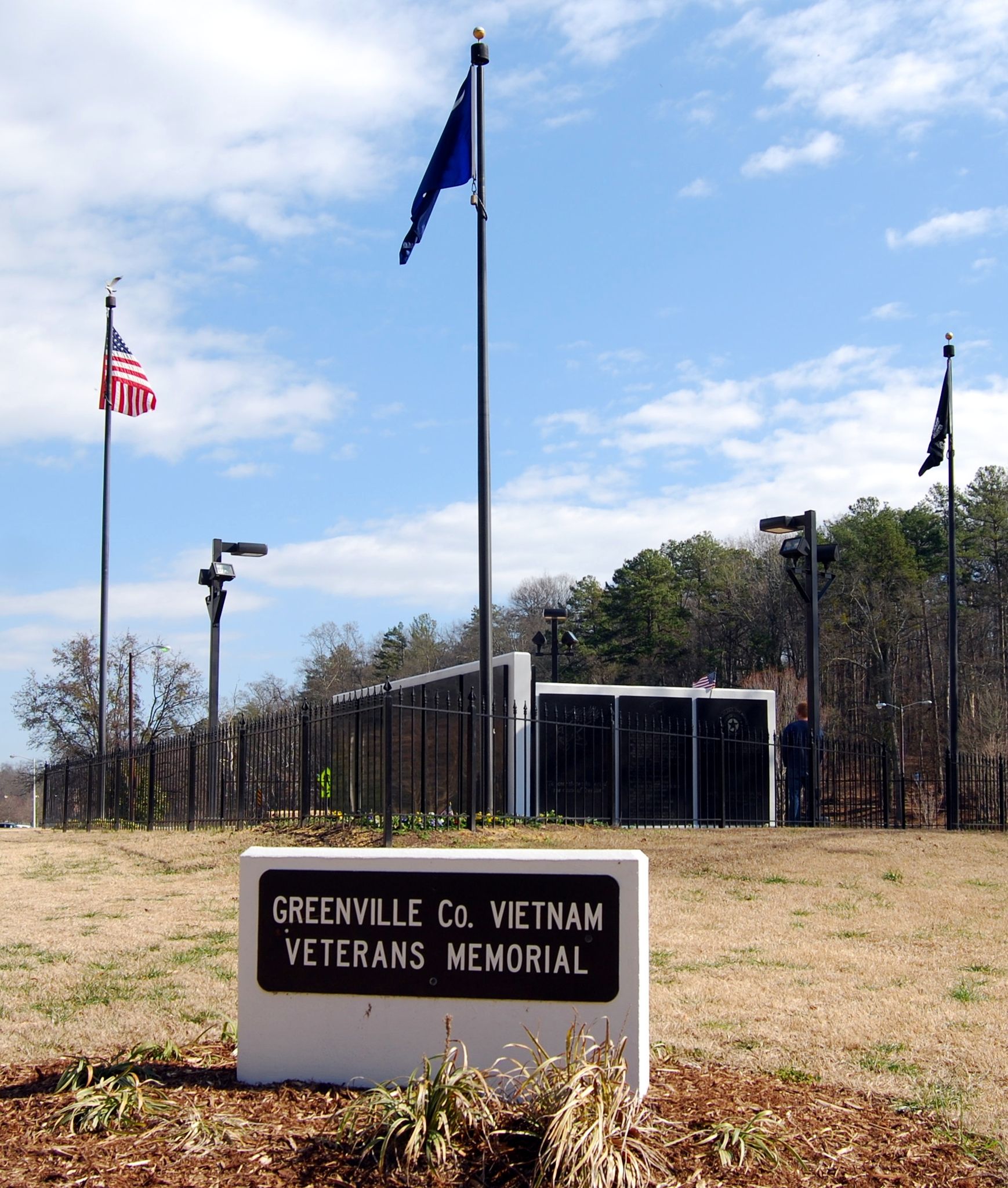 A stone memorial sign in a grassy field with flags under a cloudy sky. - Swamp Rabbit Trail