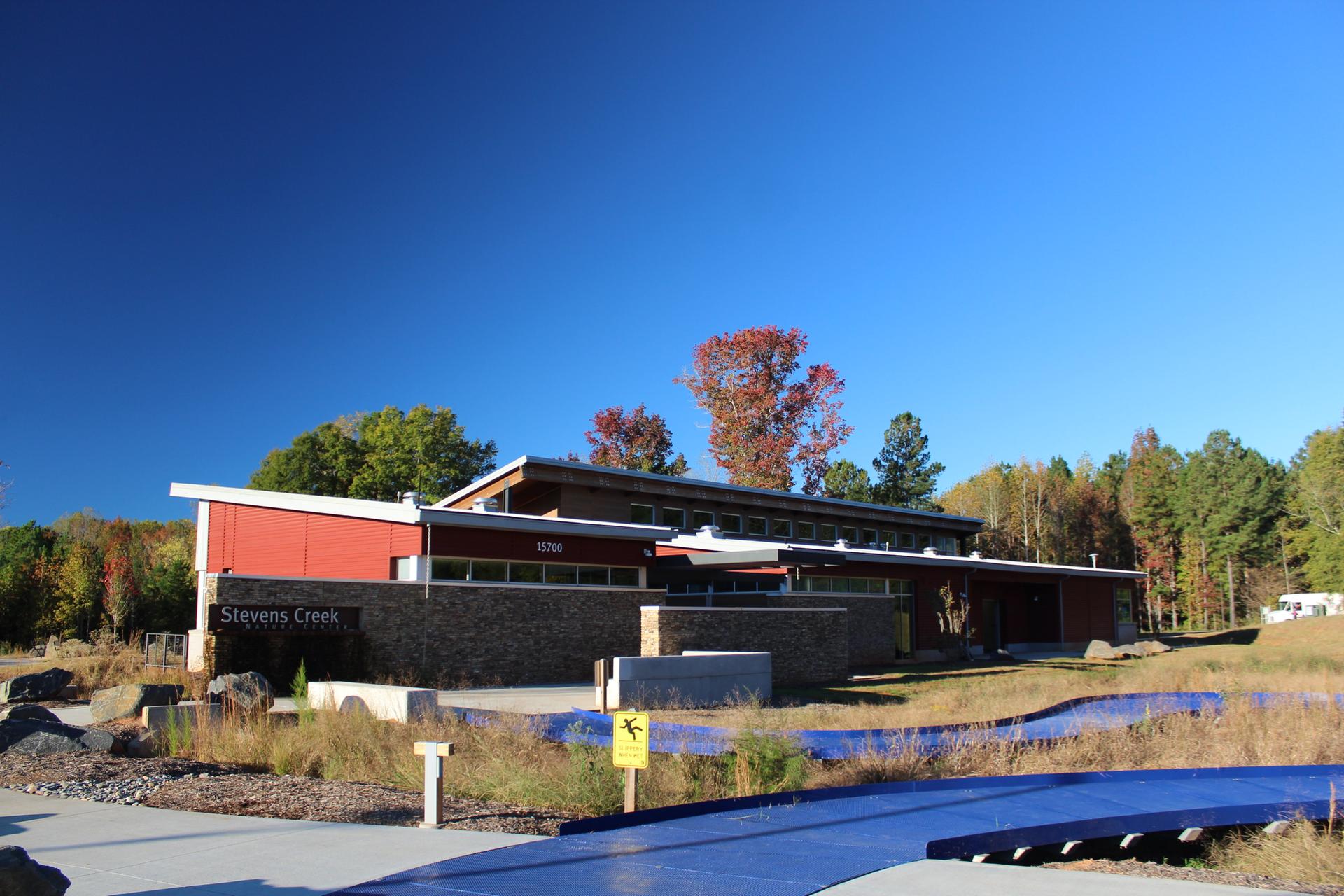 Building with red and stone walls, autumn trees, and a blue path under clear sky.
