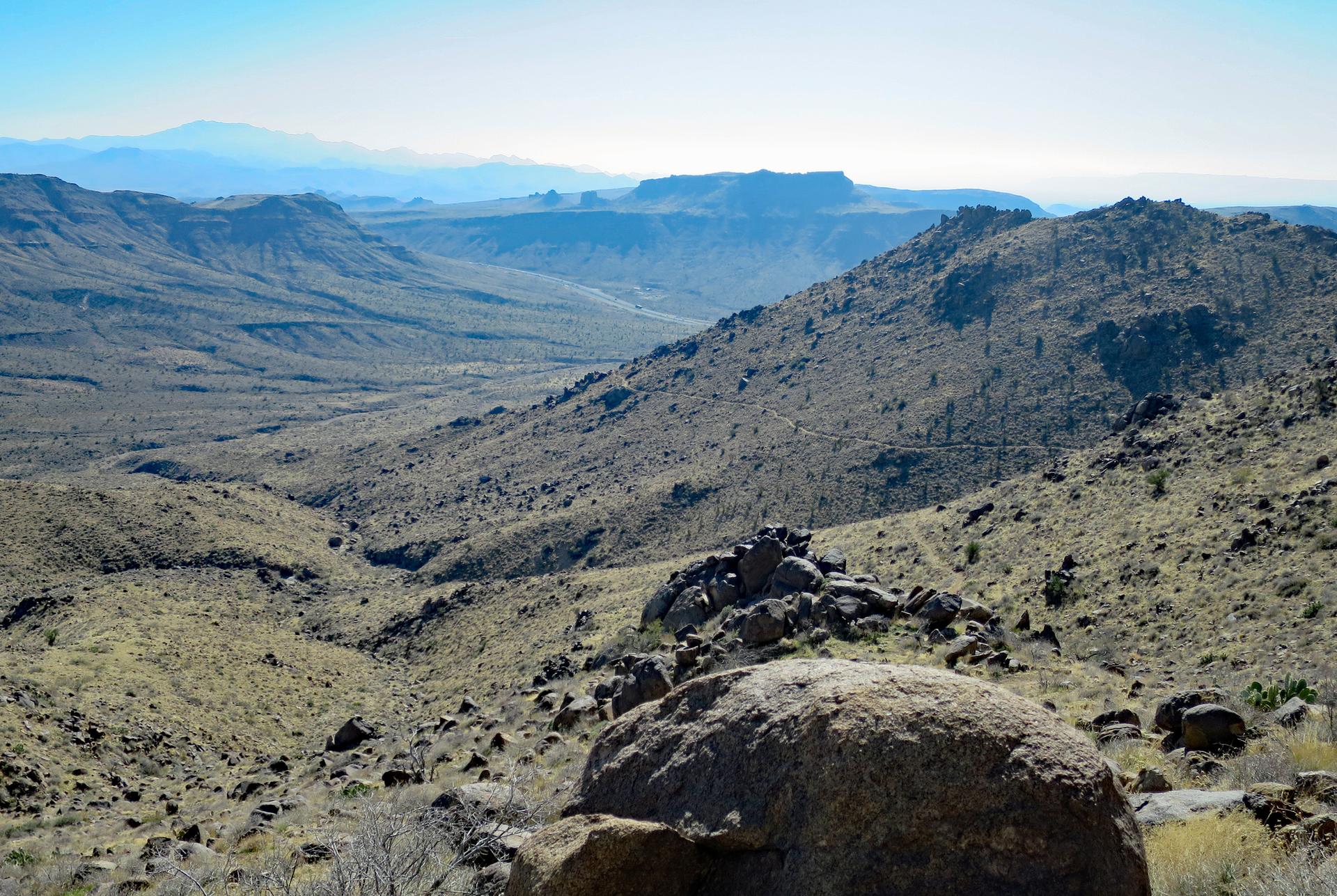 Wide view of a rugged, arid mountain range under a bright sky.