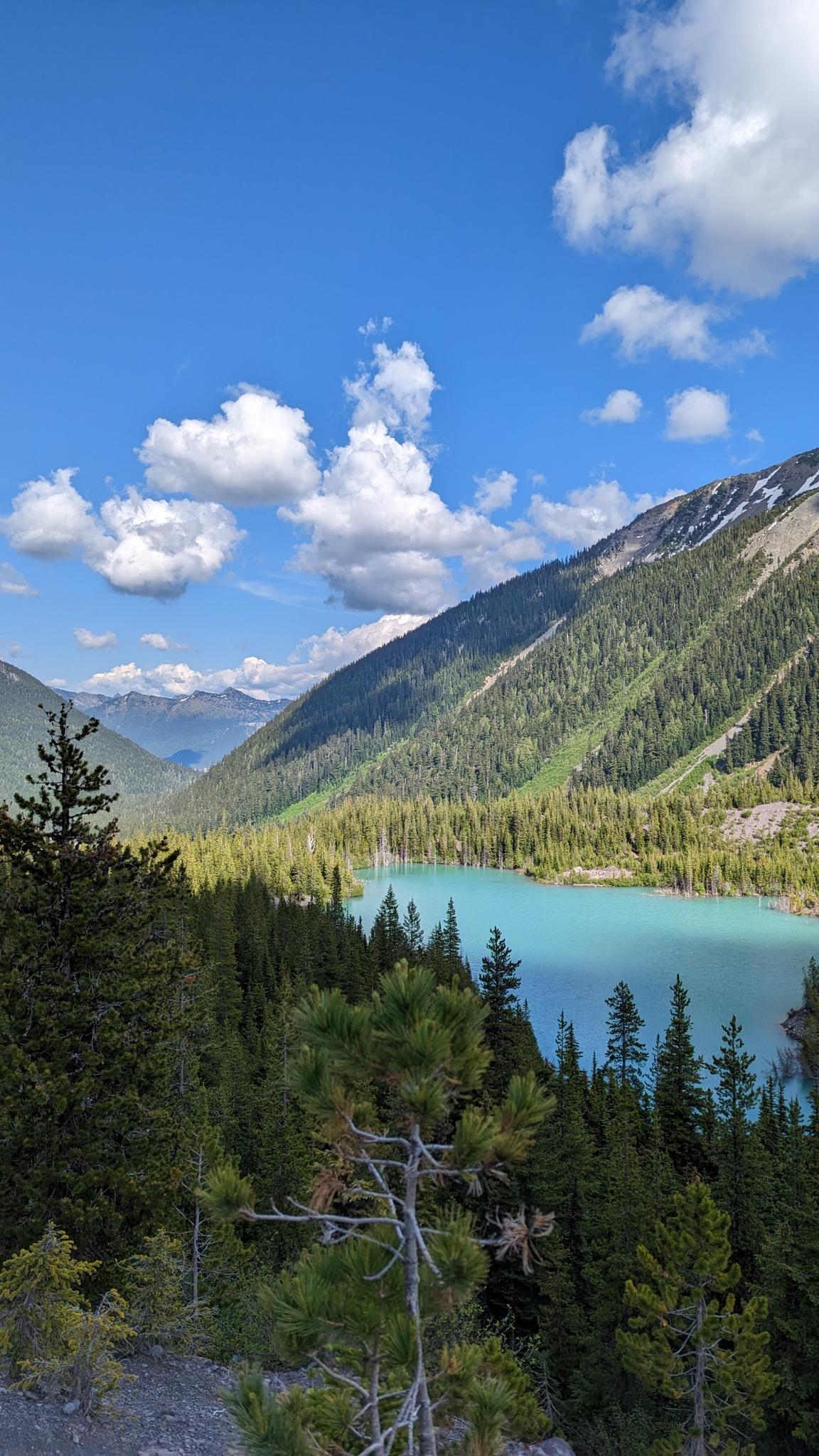 A vibrant turquoise lake nestled in a forested mountain valley under a blue sky.