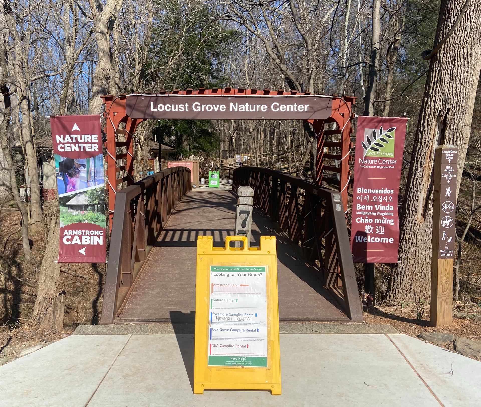 Wooden bridge entrance with informational banners and a yellow sign on a clear day.