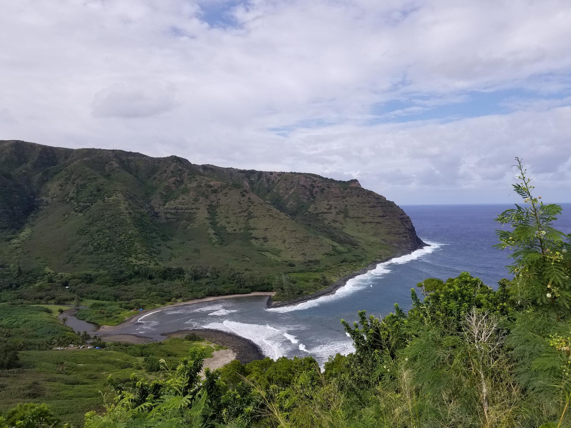 A dramatic coastal landscape with green mountains, a bay, and ocean waves.