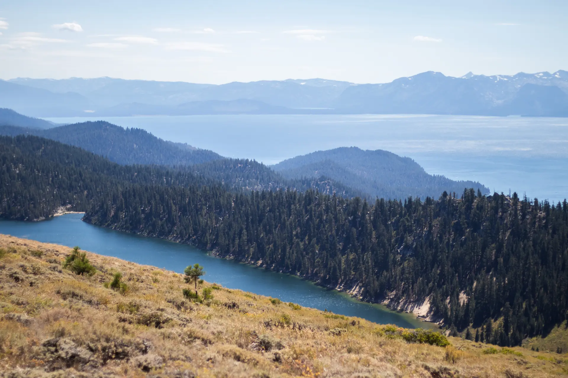 Expansive view of two blue lakes nestled among forested hills and distant mountains.