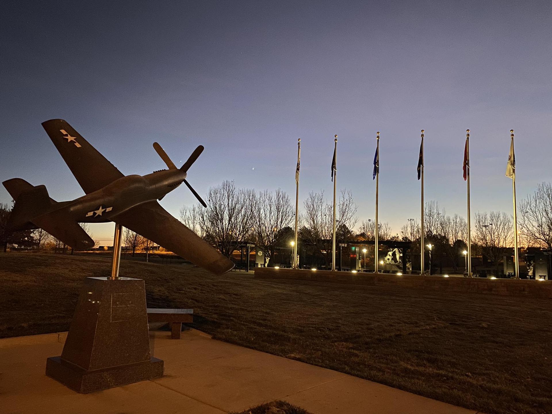 Model airplane statue and flagpoles illuminated at twilight against a dark sky.
