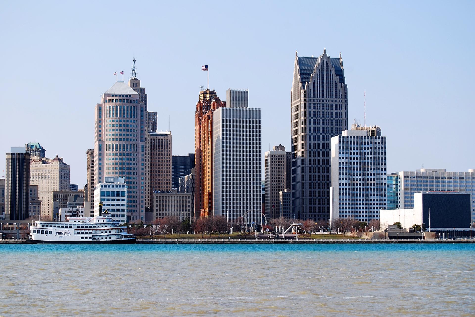 A bright city skyline with tall buildings and a large white boat on the water.