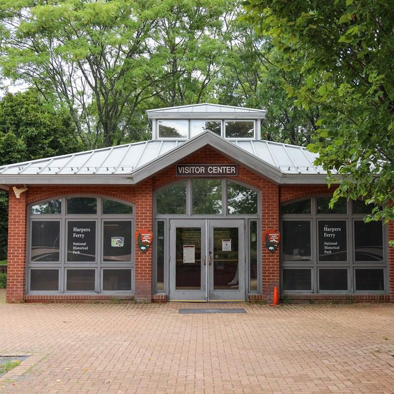 A brick visitor center building with large windows is surrounded by trees.