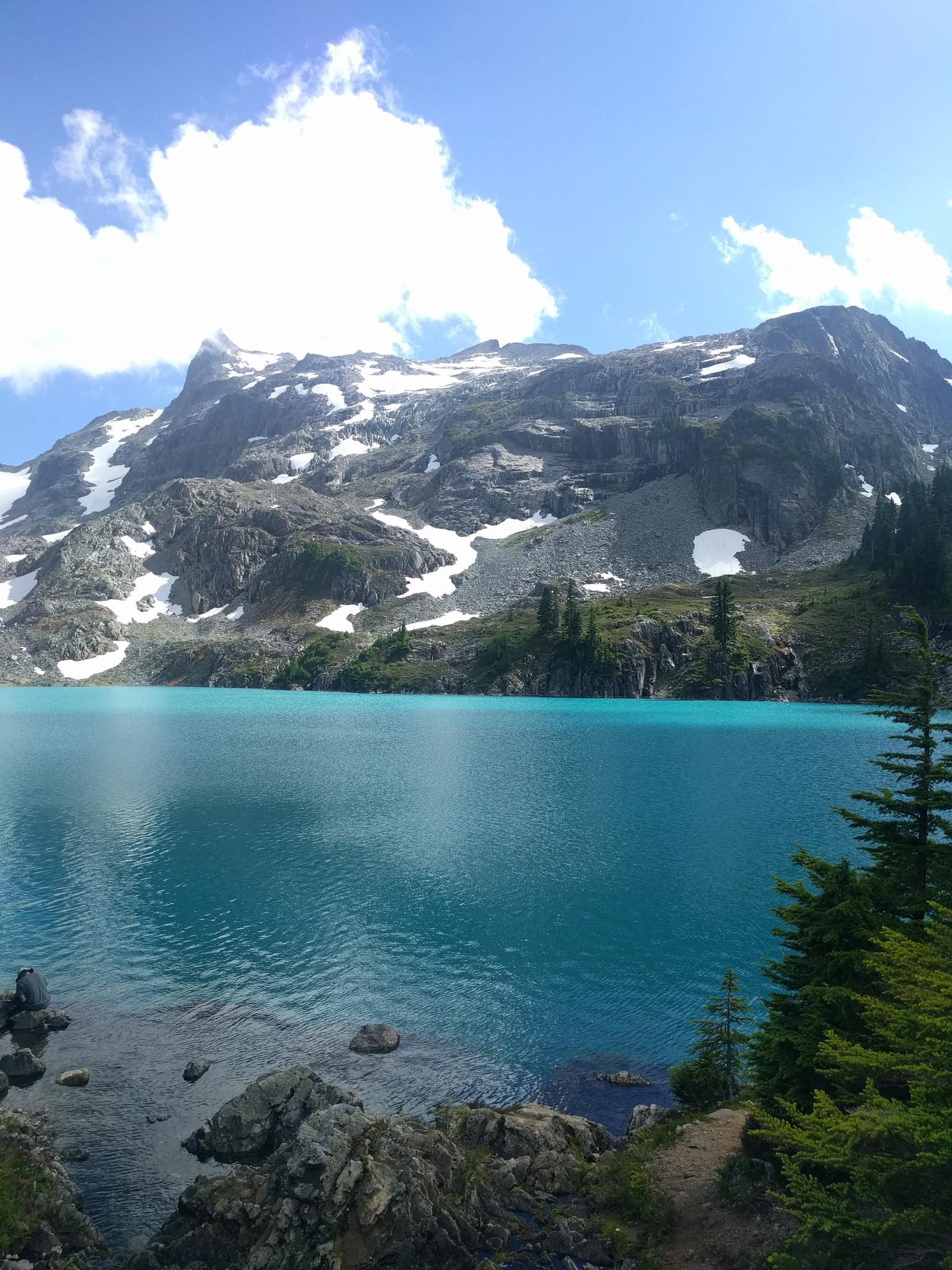 Bright turquoise alpine lake with snow-capped mountains under a sunny sky.