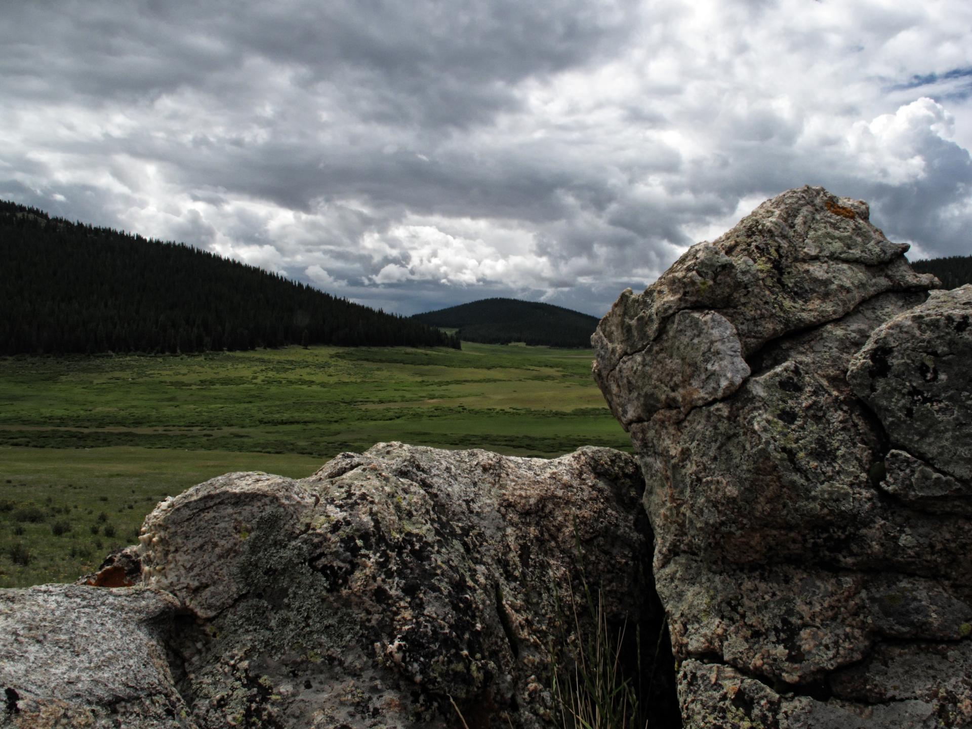 Large textured rocks in foreground overlooking a green field under cloudy skies.