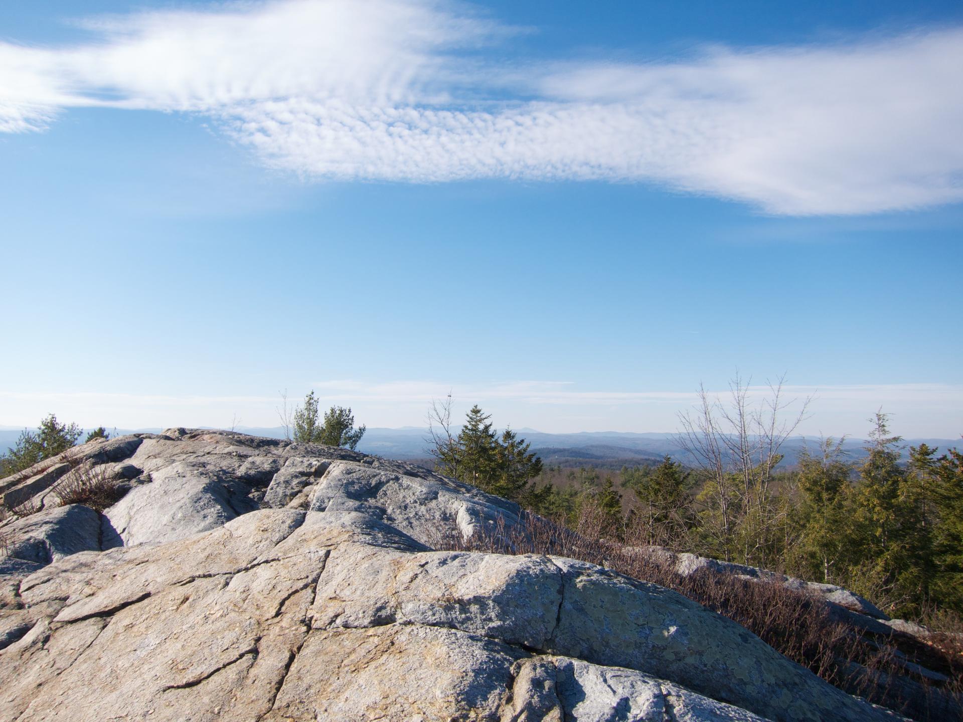 Rocky outcrop overlooking a vast forested landscape under a bright blue sky.