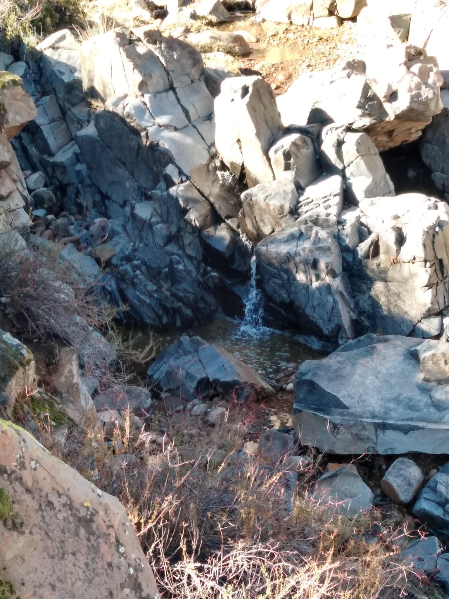 Small waterfall cascading into a rocky pool amidst large boulders.