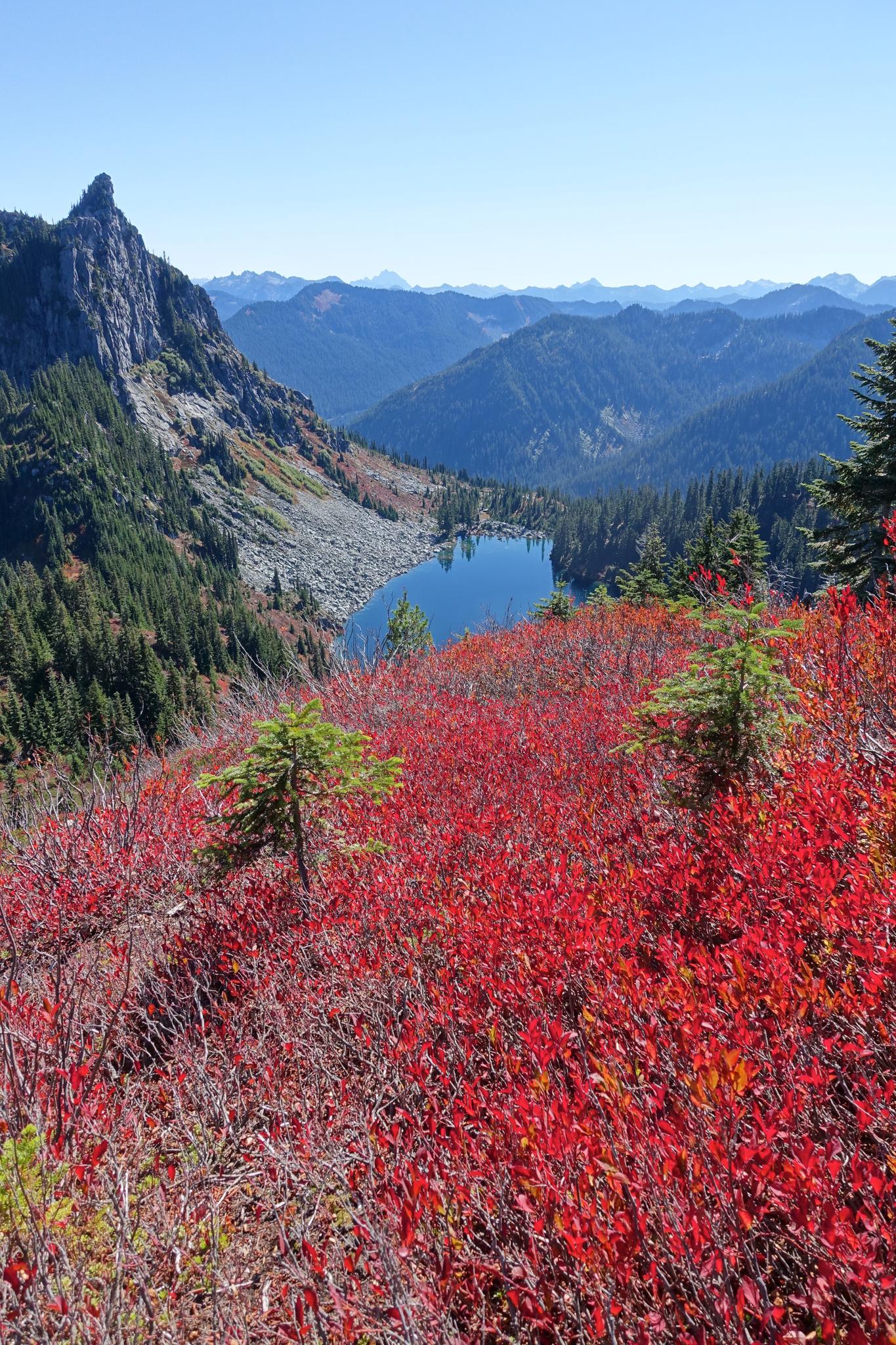 Vibrant red autumn foliage overlooks a serene blue mountain lake under clear skies.