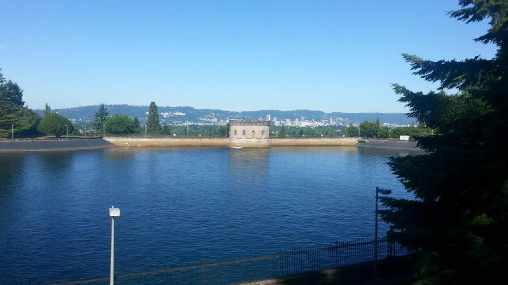 Sunny view of a large reservoir with a building and distant city.