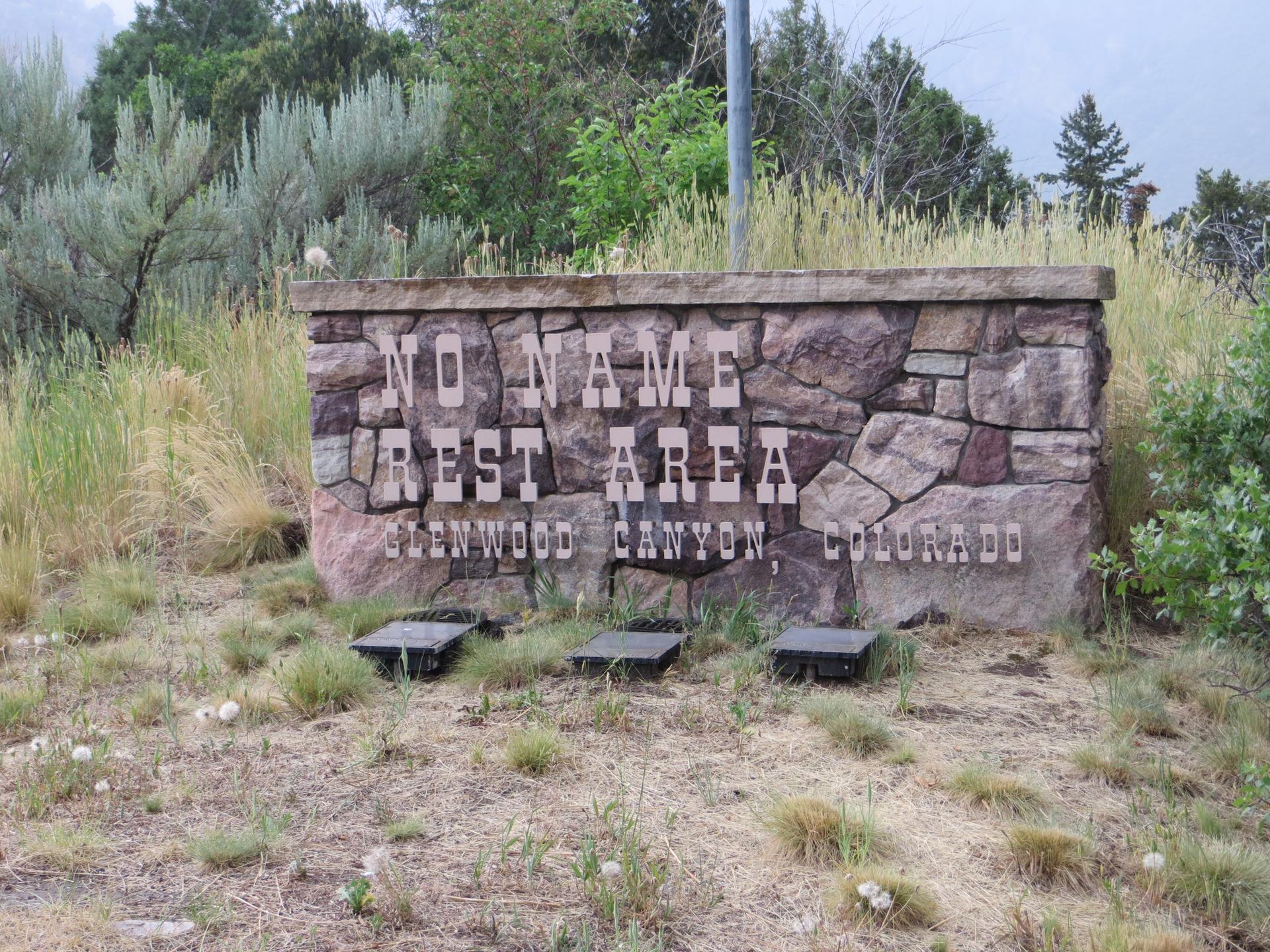Stone sign for a rest area, surrounded by dry grass and shrubs.