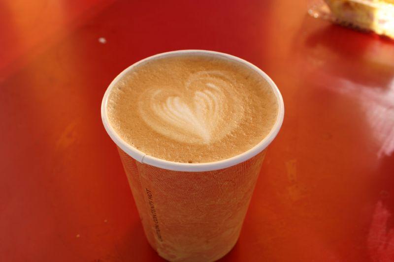 A close-up of a coffee cup with a heart-shaped latte art on a red surface.