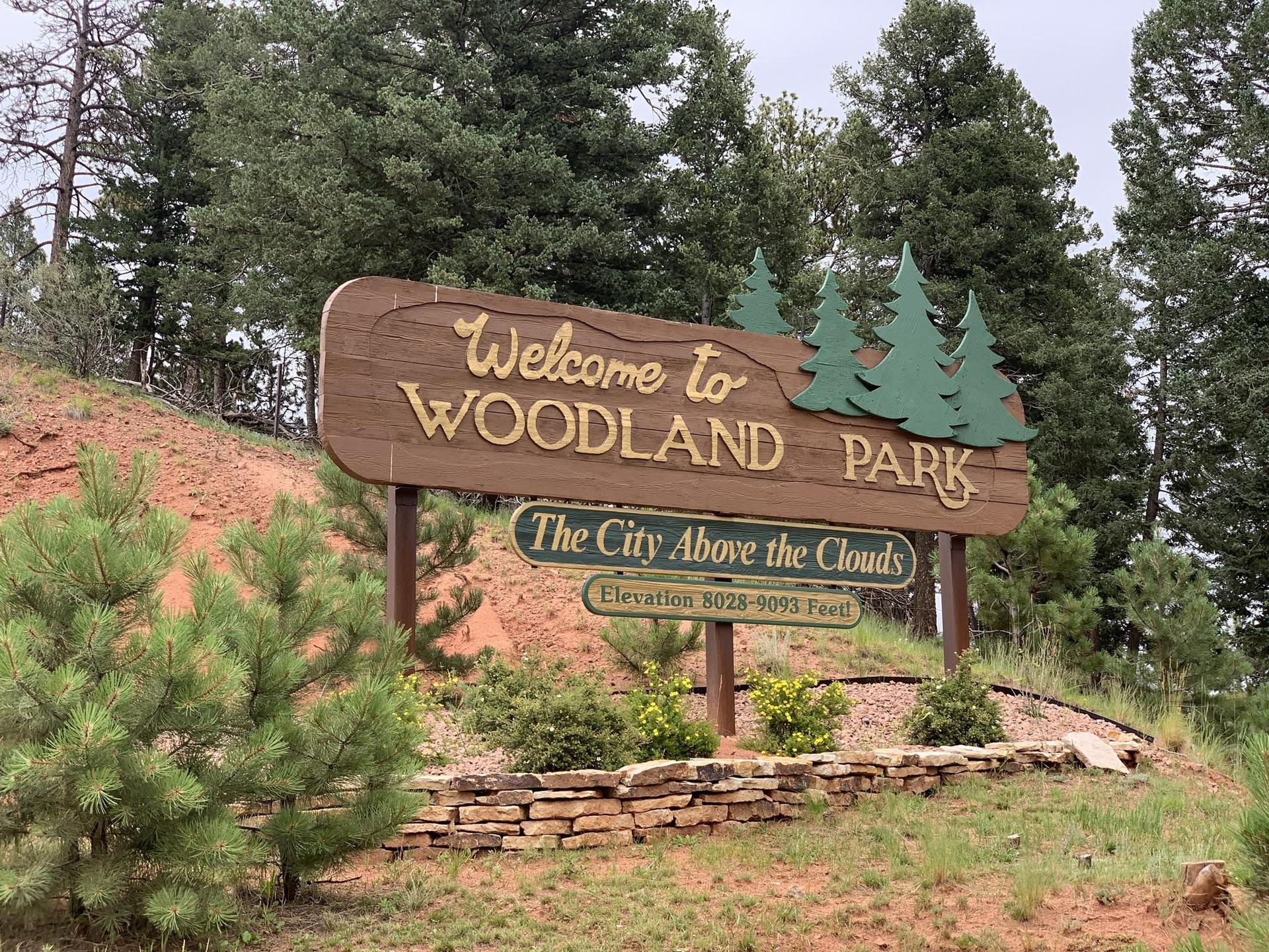 A large wooden welcome sign with pine trees on a hillside.