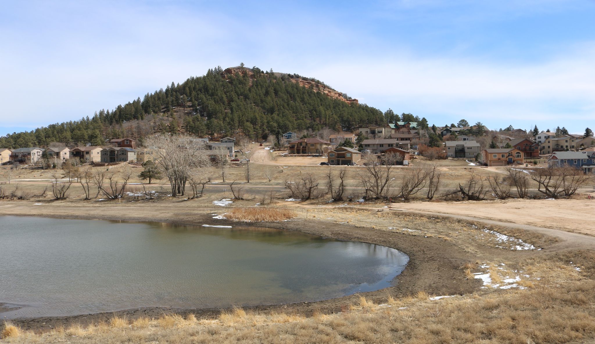 A lake with dry grass, houses, and a forested hill under a bright sky. - Ben Lomand Mountain loop run