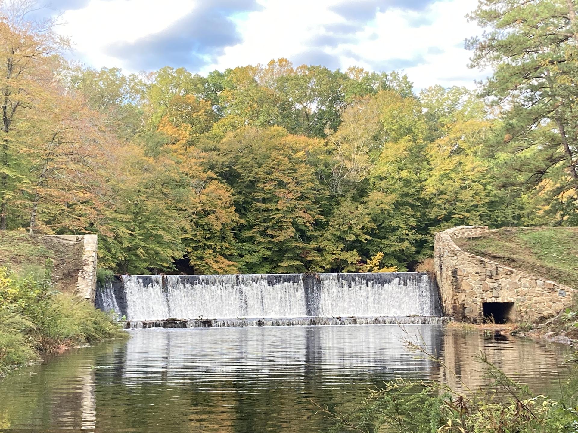 Wide waterfall over a river, surrounded by vibrant autumn trees.