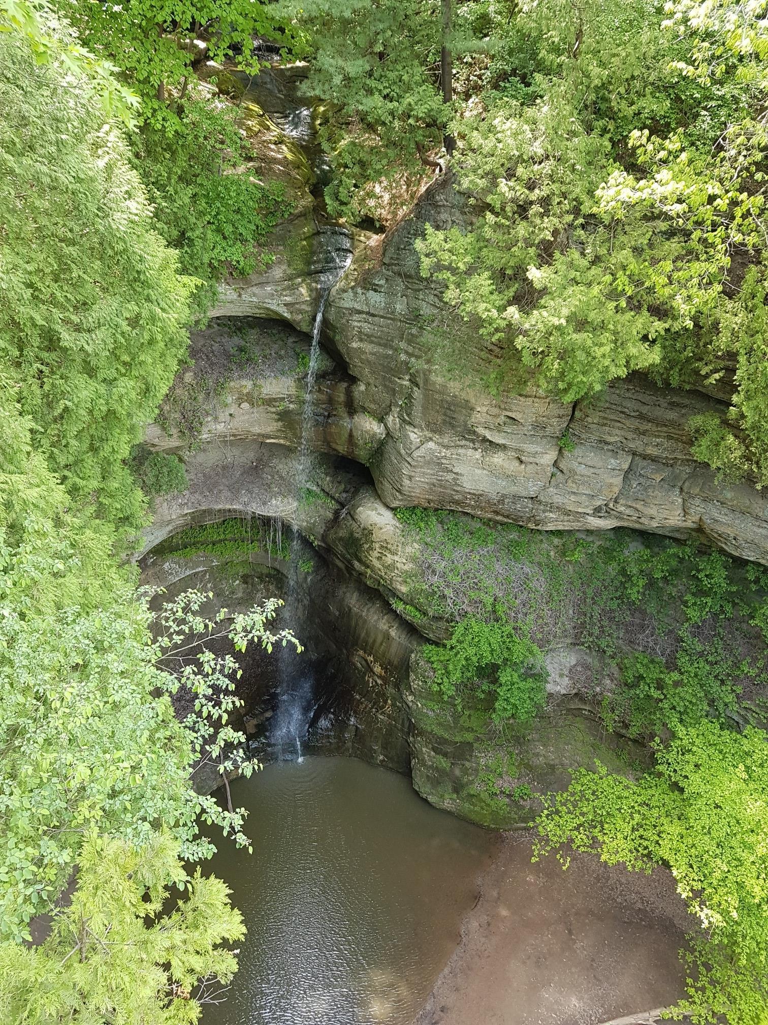 Narrow waterfall cascading into a green, rocky gorge from above.