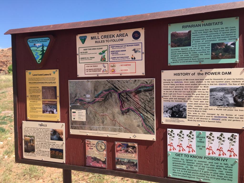 Brown informational sign with multiple panels under a bright sky.