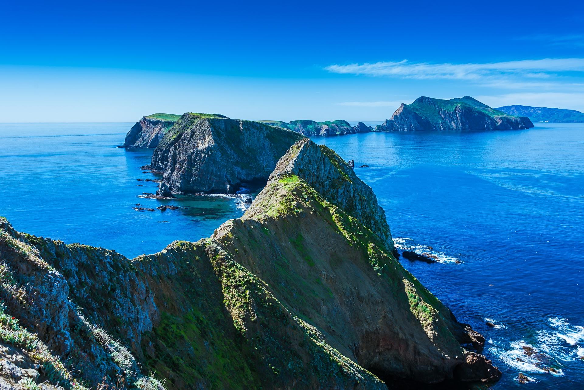 Dramatic green and rocky islands rise from a deep blue ocean.